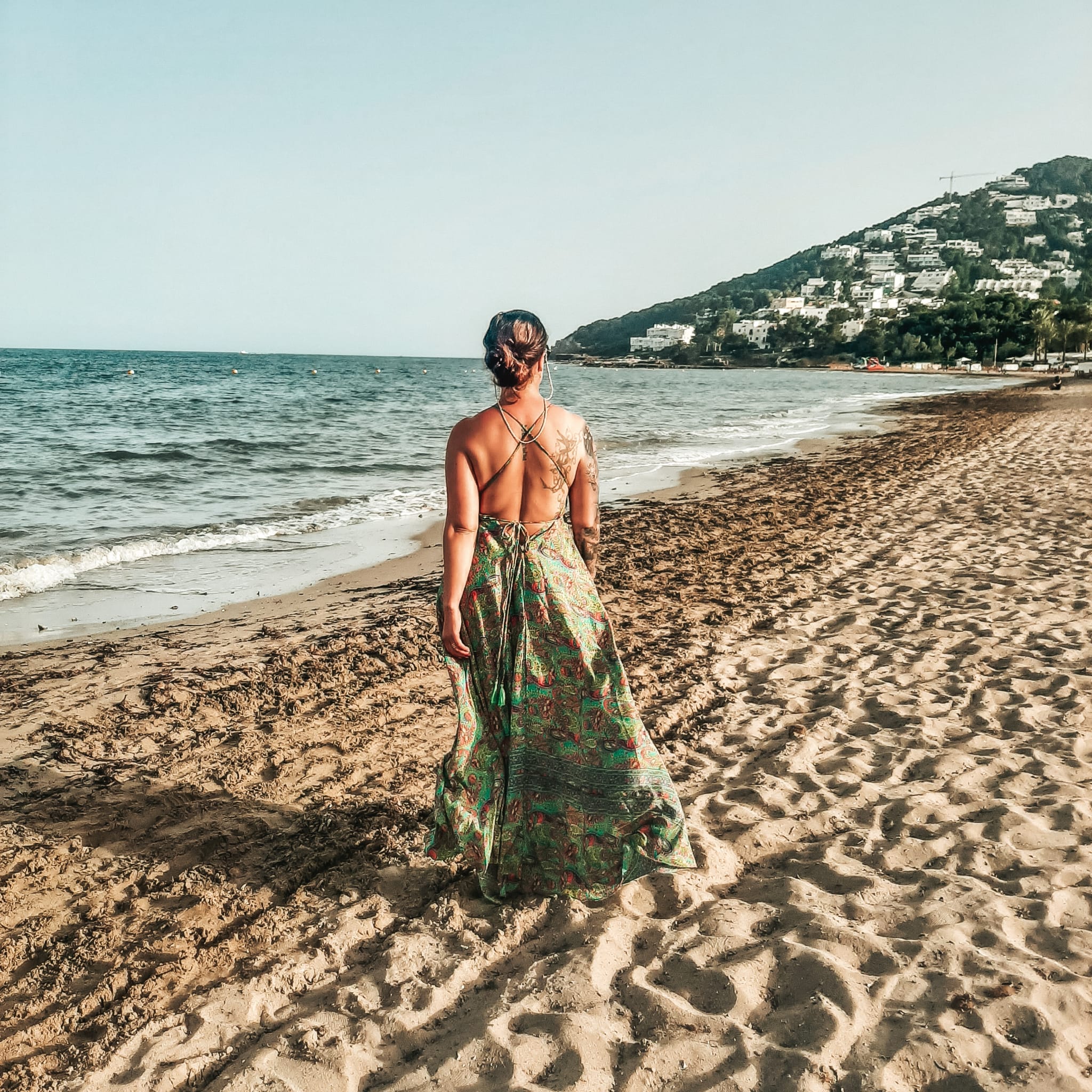 Joyce Scheeper van Magician Coaching loopt van de camera weg op het strand in een groene lange jurk richting de zee.